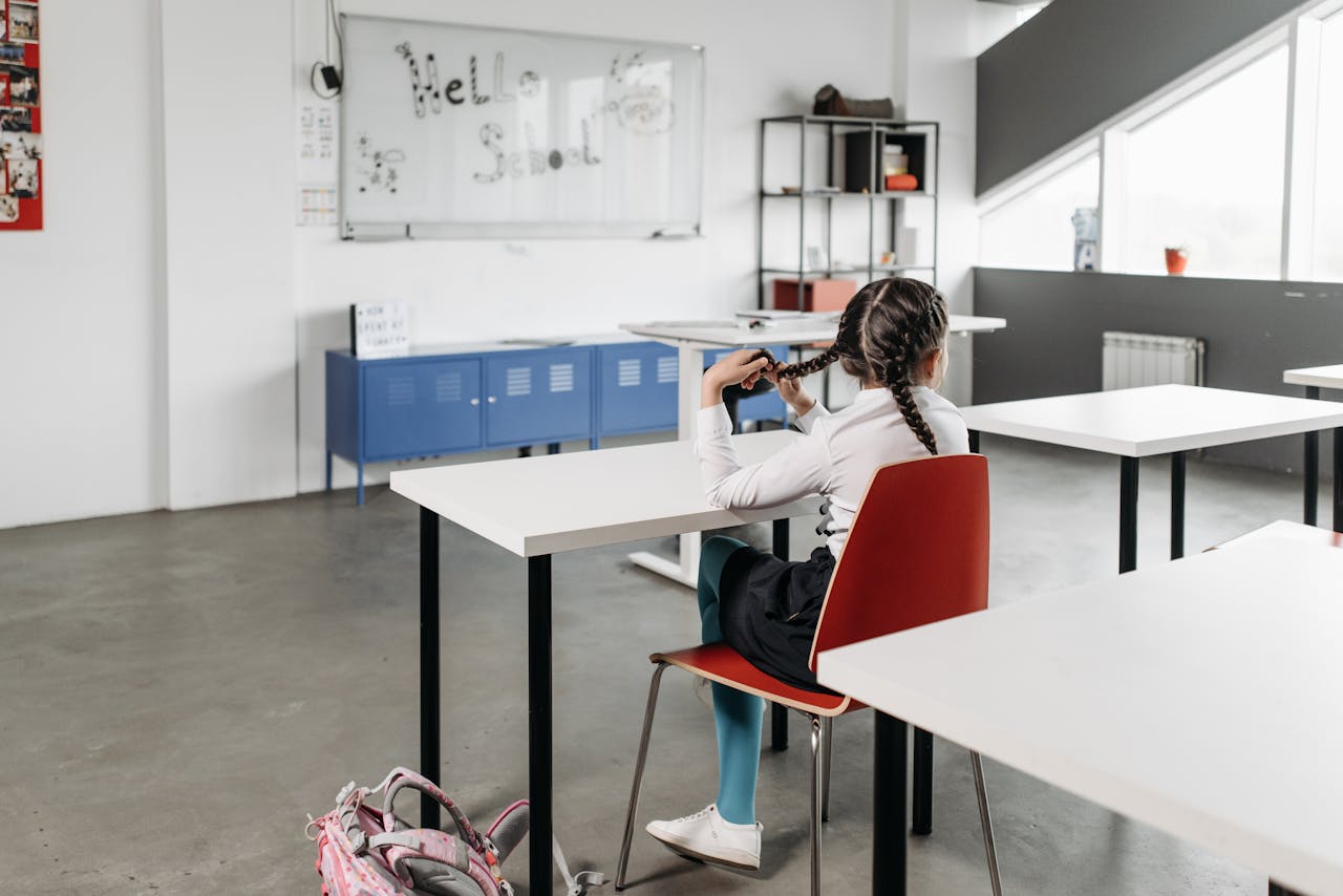 Young girl braiding hair in a bright, modern classroom. Back to school vibes.